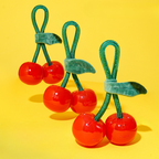 Three red cherry-shaped toys with green stems on a yellow background