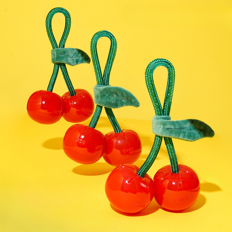 Three red cherry-shaped toys with green stems on a yellow background